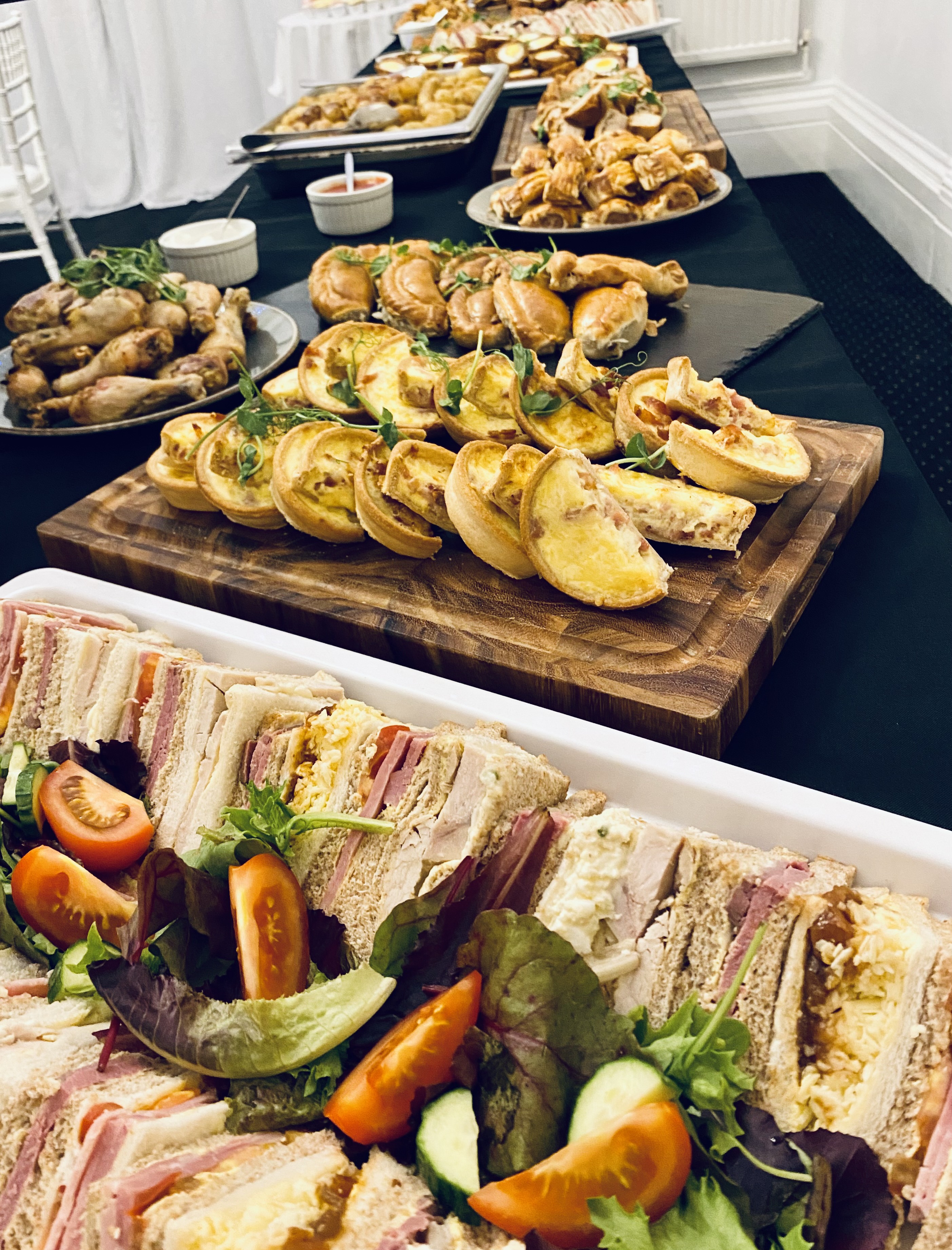 Wedding buffet of quiche, sandwiches and chicken on wooden boards